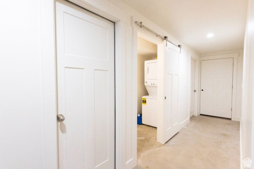 Hallway with a barn door and stacked washer and dryer