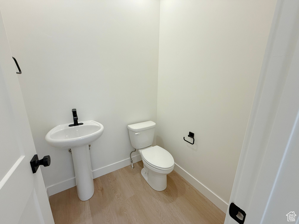 Half bath featuring wood finished floors, toilet, and baseboards