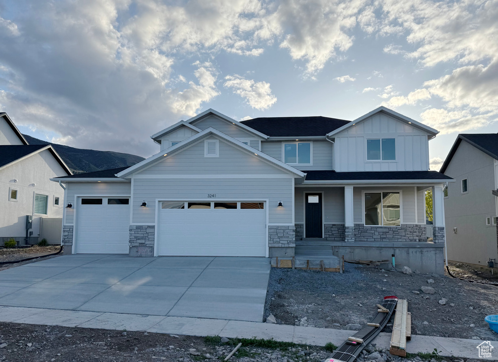 Craftsman inspired home featuring covered porch, stone siding, board and batten siding, an attached garage, and driveway
