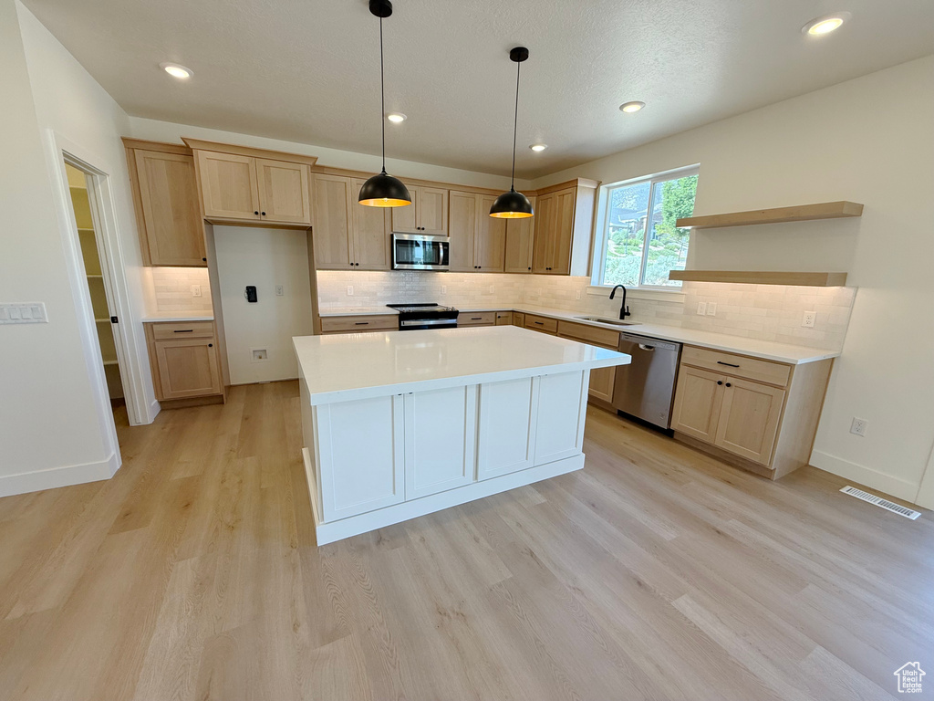 Kitchen with appliances with stainless steel finishes, a sink, open shelves, light wood-style flooring, and backsplash