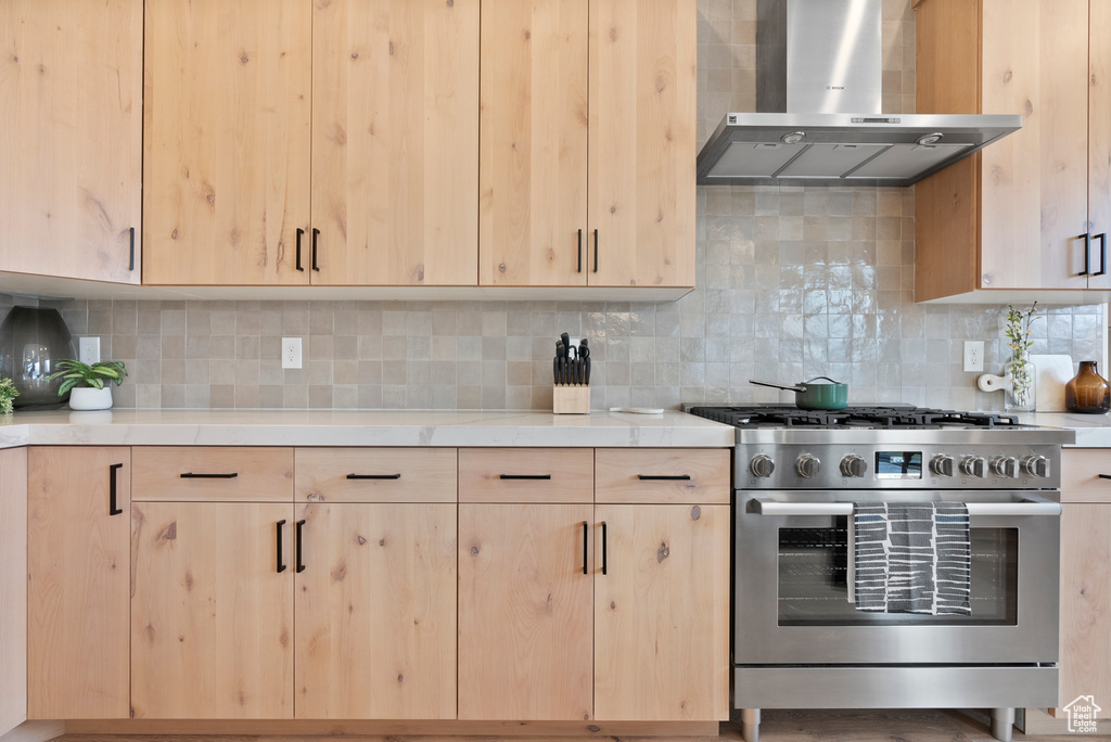 Kitchen with high end stove, tasteful backsplash, and wall chimney exhaust hood