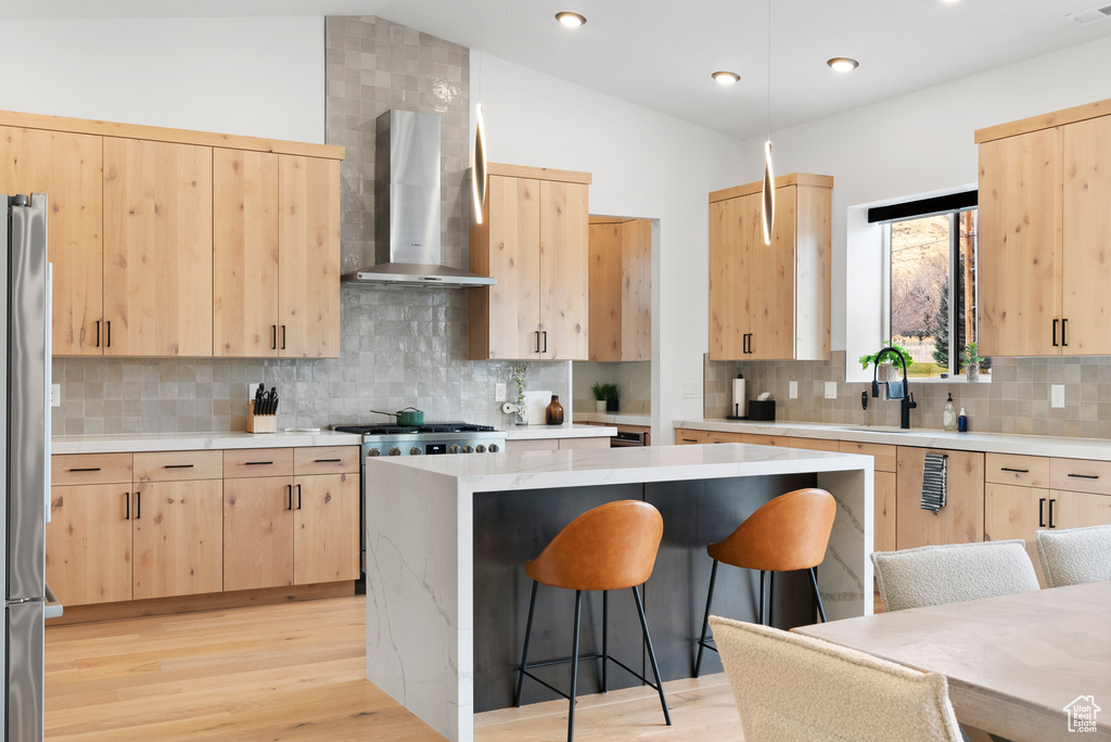 Kitchen featuring wall chimney exhaust hood, a kitchen breakfast bar, vaulted ceiling, decorative backsplash, and light brown cabinetry