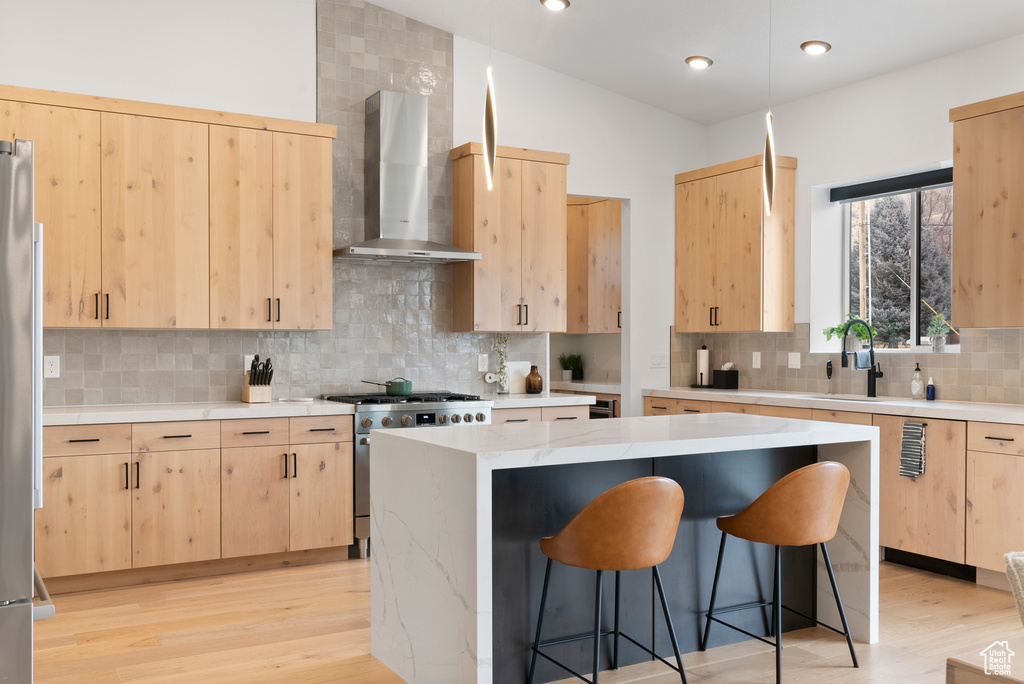 Kitchen with appliances with stainless steel finishes, tasteful backsplash, wall chimney range hood, light brown cabinets, and a center island