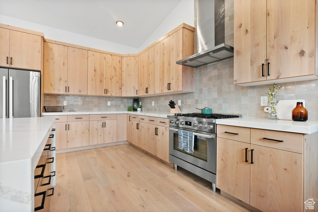 Kitchen featuring backsplash, wall chimney range hood, light hardwood / wood-style flooring, light brown cabinetry, and stainless steel appliances