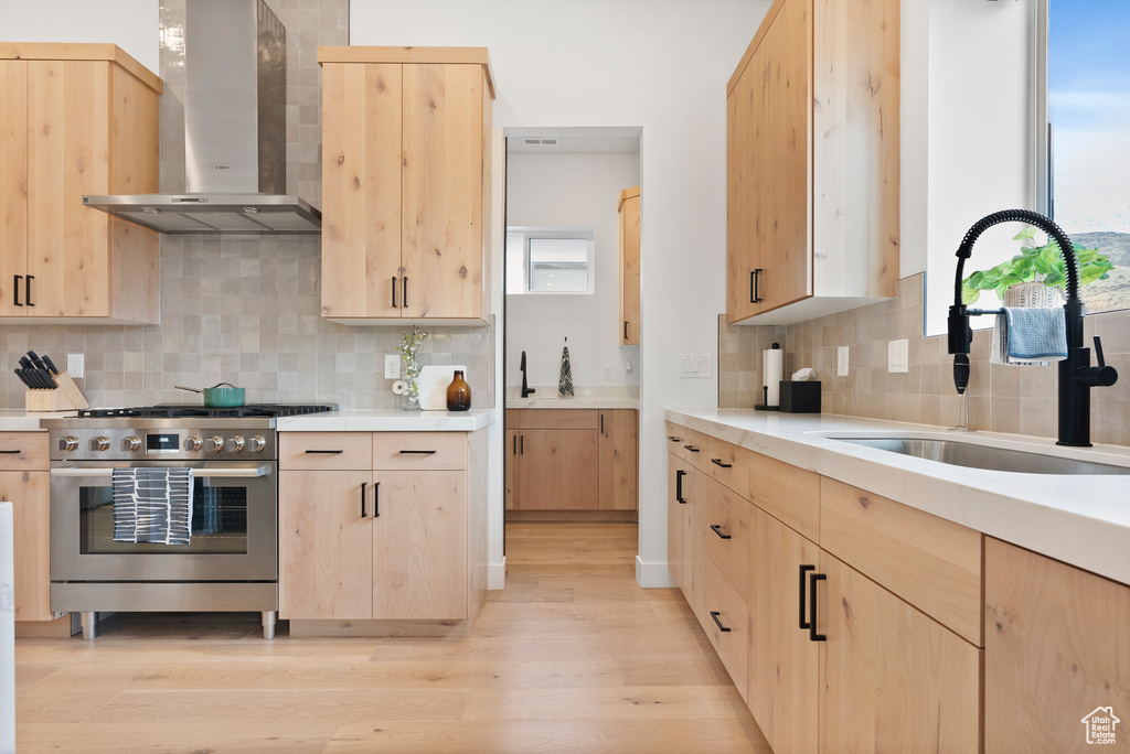 Kitchen with wall chimney range hood, sink, and light brown cabinetry