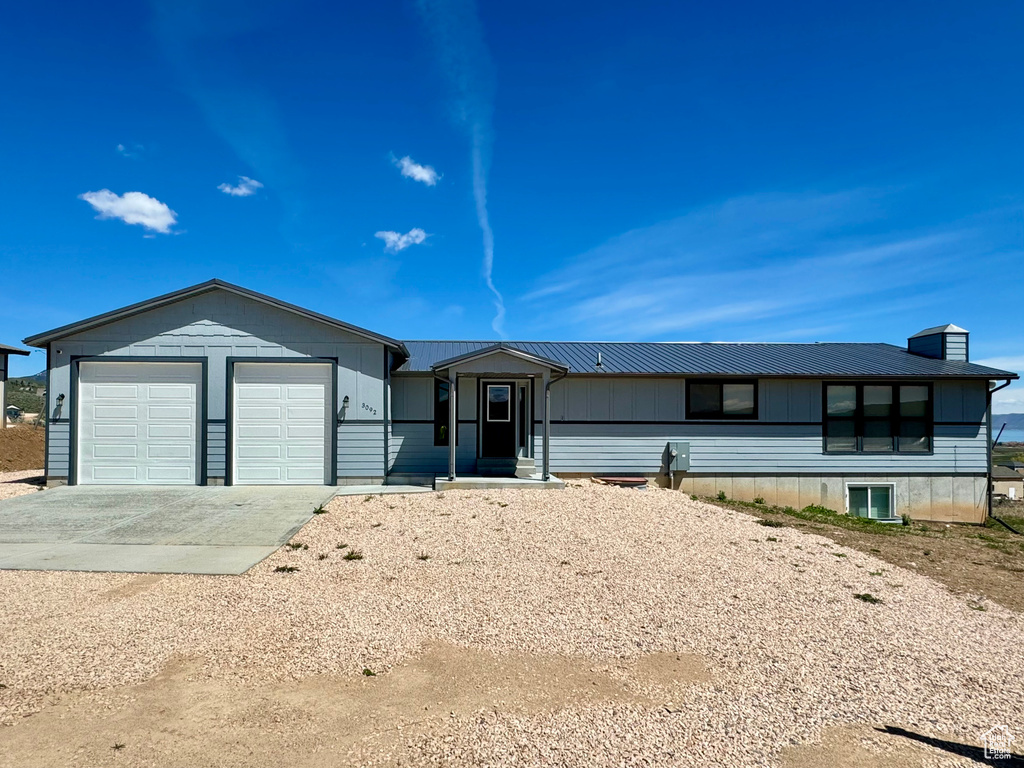 Ranch-style home featuring concrete driveway, a metal roof, an attached garage, and a chimney