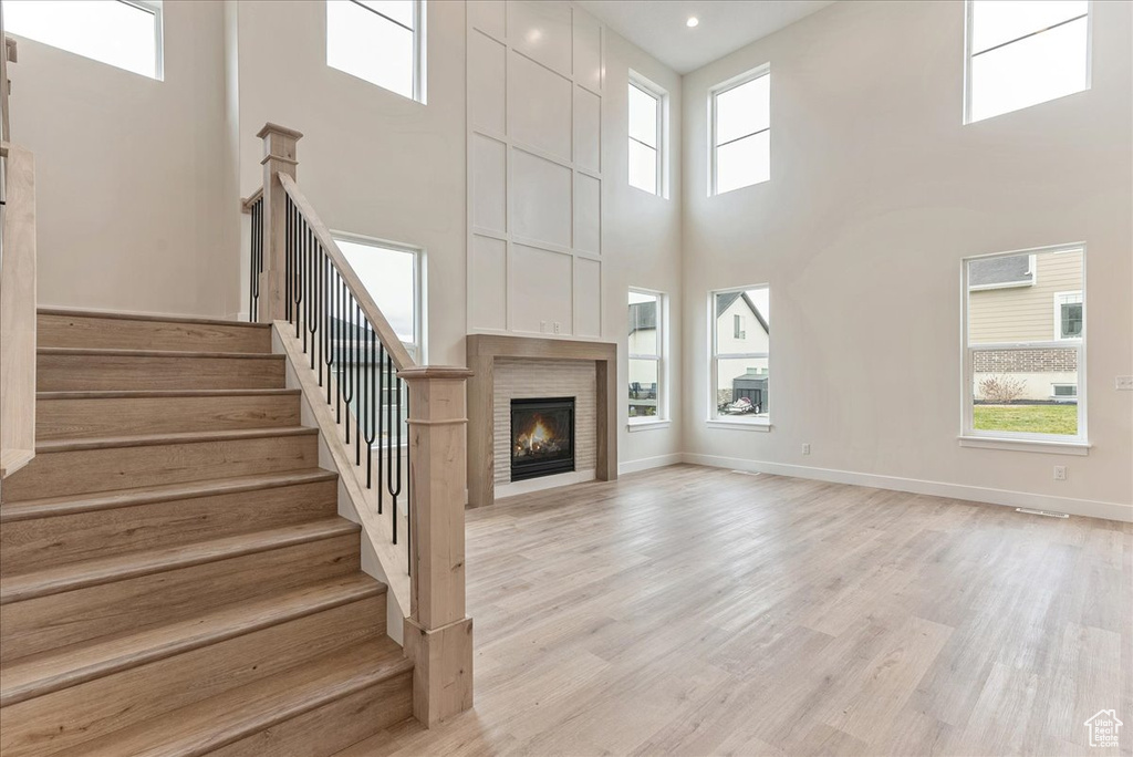 Unfurnished living room featuring a towering ceiling, a healthy amount of sunlight, and light wood-type flooring