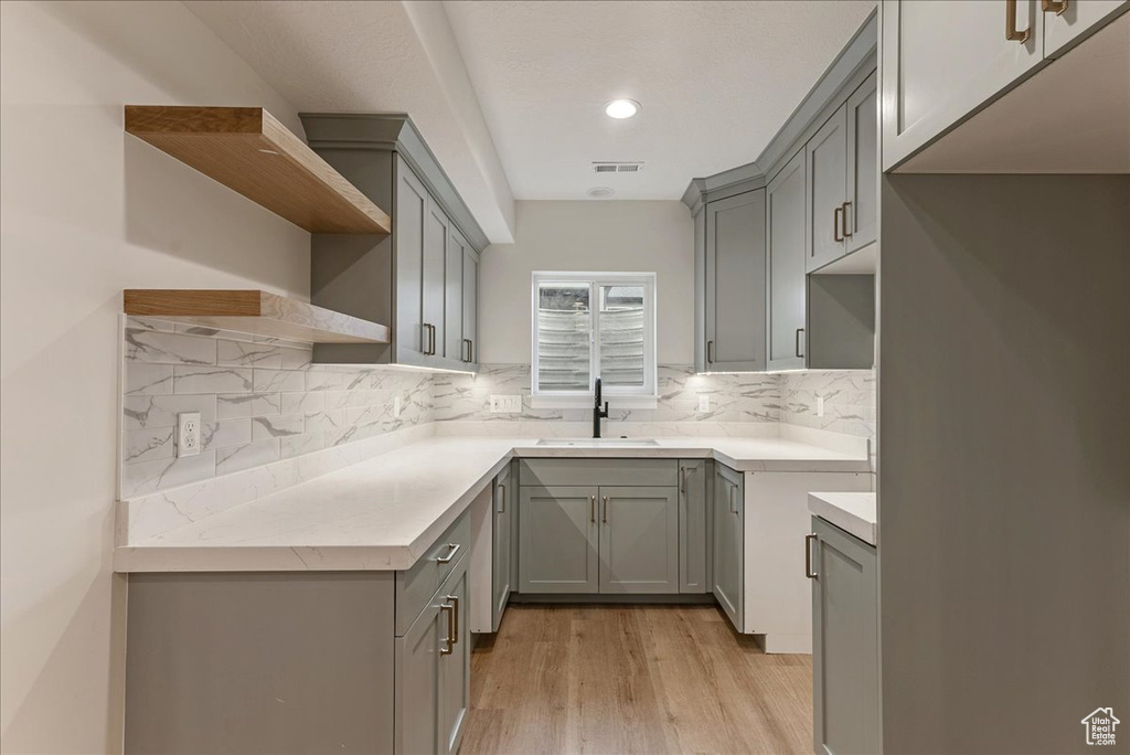 Kitchen featuring gray cabinets, decorative backsplash, sink, and light hardwood / wood-style flooring