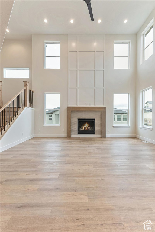 Unfurnished living room featuring ceiling fan, light hardwood / wood-style floors, and a high ceiling