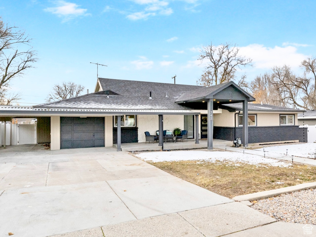 View of front of house featuring driveway, an attached carport, roof with shingles, an attached garage, and fence