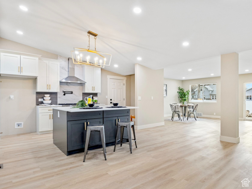 Kitchen featuring wall chimney exhaust hood, a kitchen island, white cabinetry, and vaulted ceiling