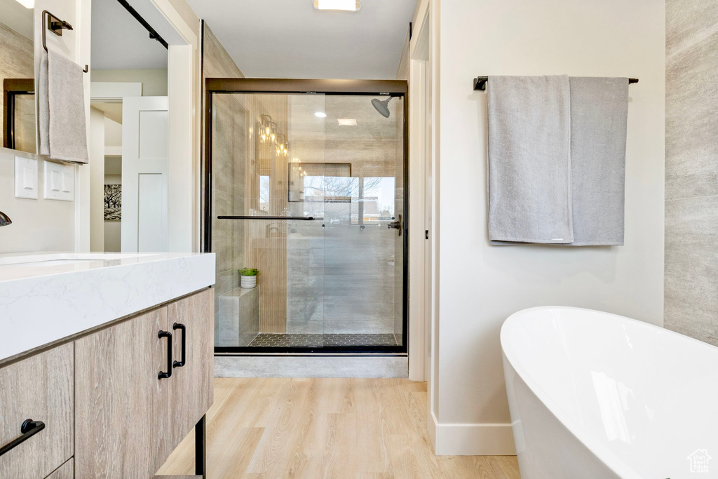 Bathroom with a stall shower, baseboards, a soaking tub, wood finished floors, and vanity