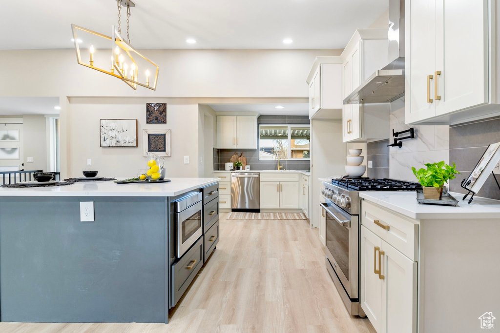 Kitchen featuring light countertops, appliances with stainless steel finishes, wall chimney range hood, and white cabinetry