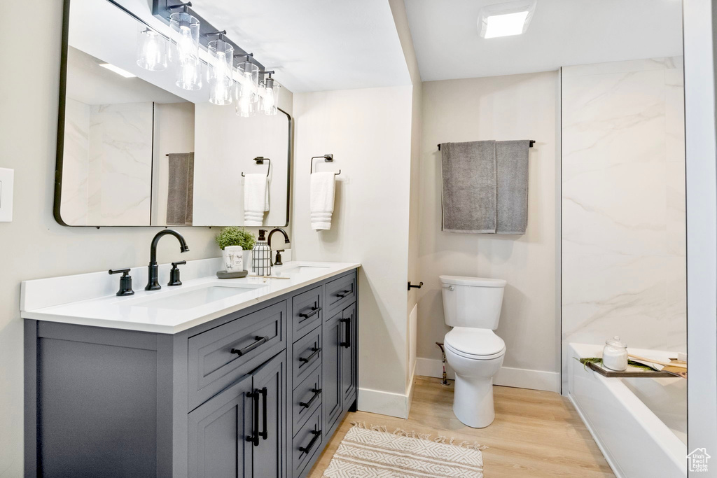 Full bath with double vanity, wood finished floors, a sink, and toilet