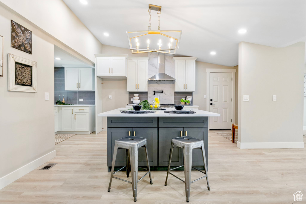 Kitchen featuring light wood-style floors, wall chimney exhaust hood, white cabinetry, and light countertops