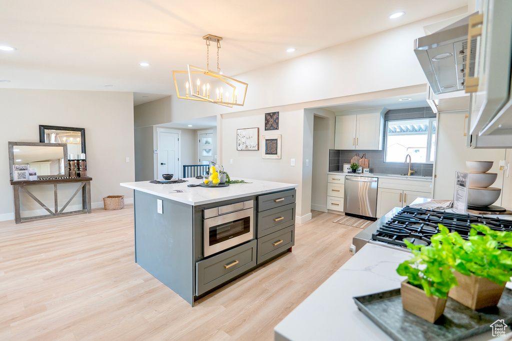 Kitchen with light wood finished floors, tasteful backsplash, built in microwave, stainless steel dishwasher, and a sink