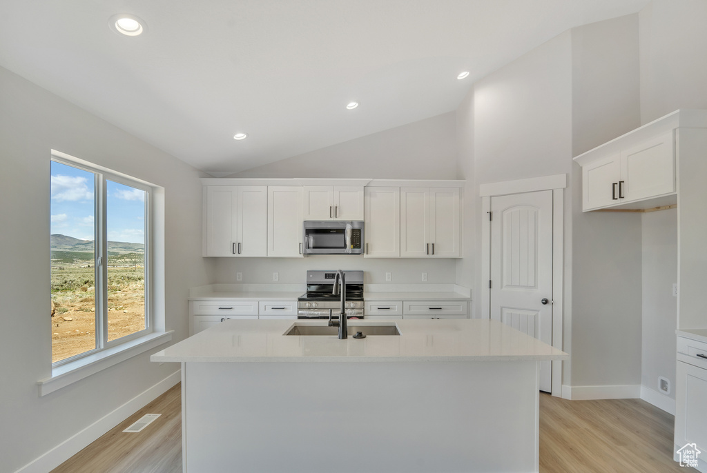 Kitchen with vaulted ceiling, a sink, an island with sink, visible vents, and appliances with stainless steel finishes
