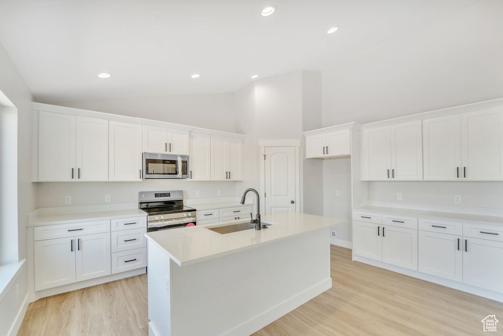 Kitchen featuring lofted ceiling, stainless steel appliances, a sink, an island with sink, and light wood finished floors