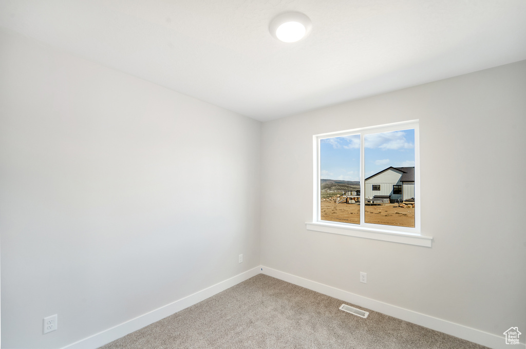 Empty room featuring baseboards, visible vents, and light carpet