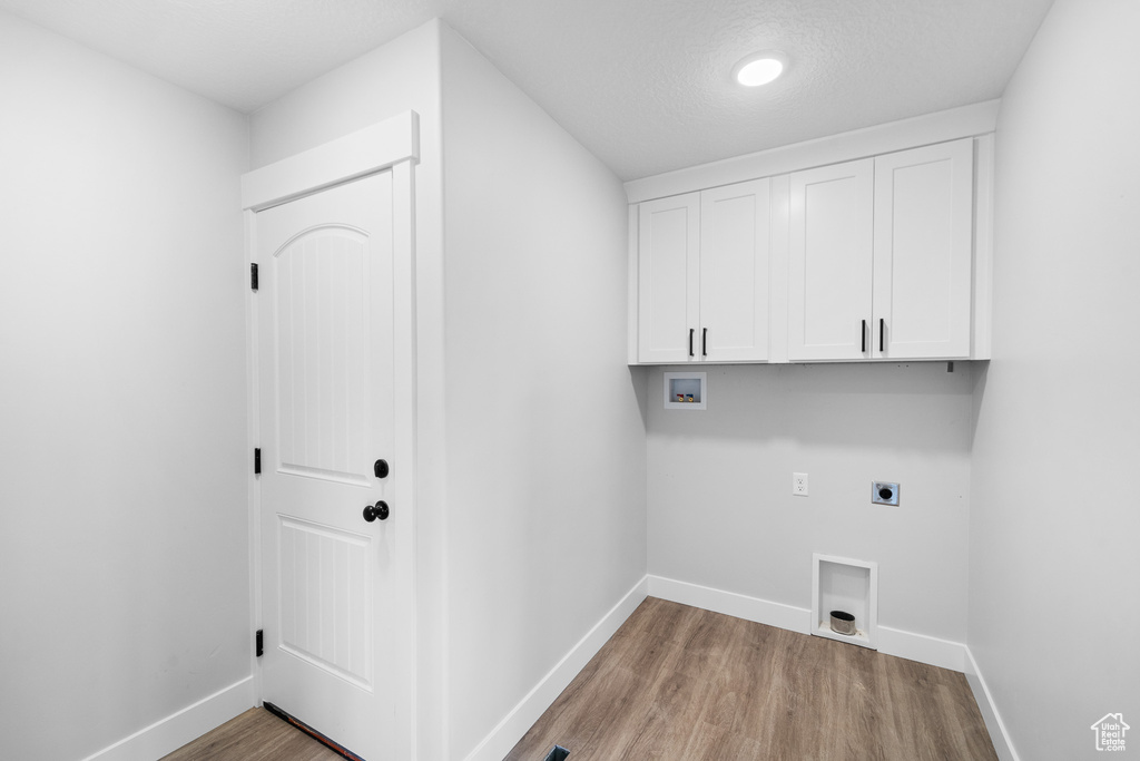 Laundry area with a textured ceiling, cabinets, electric dryer hookup, hookup for a washing machine, and light hardwood / wood-style flooring