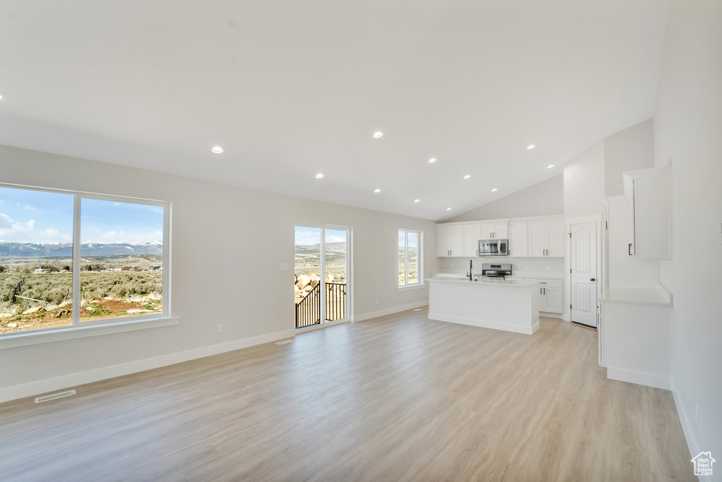 Unfurnished living room with recessed lighting, high vaulted ceiling, baseboards, light wood finished floors, and visible vents