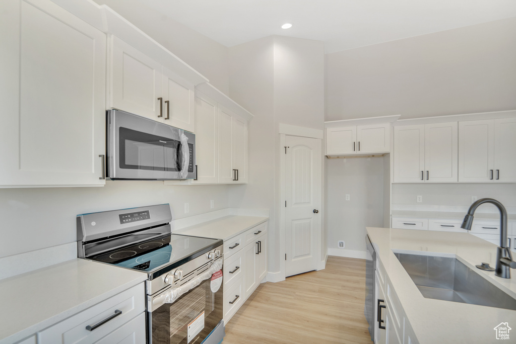 Kitchen with a sink, white cabinetry, light wood-type flooring, and appliances with stainless steel finishes