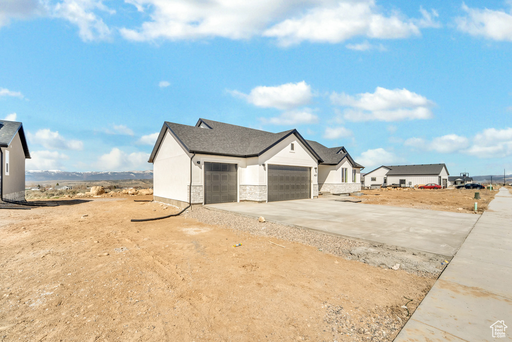 View of front facade featuring driveway, stone siding, roof with shingles, stucco siding, and a garage
