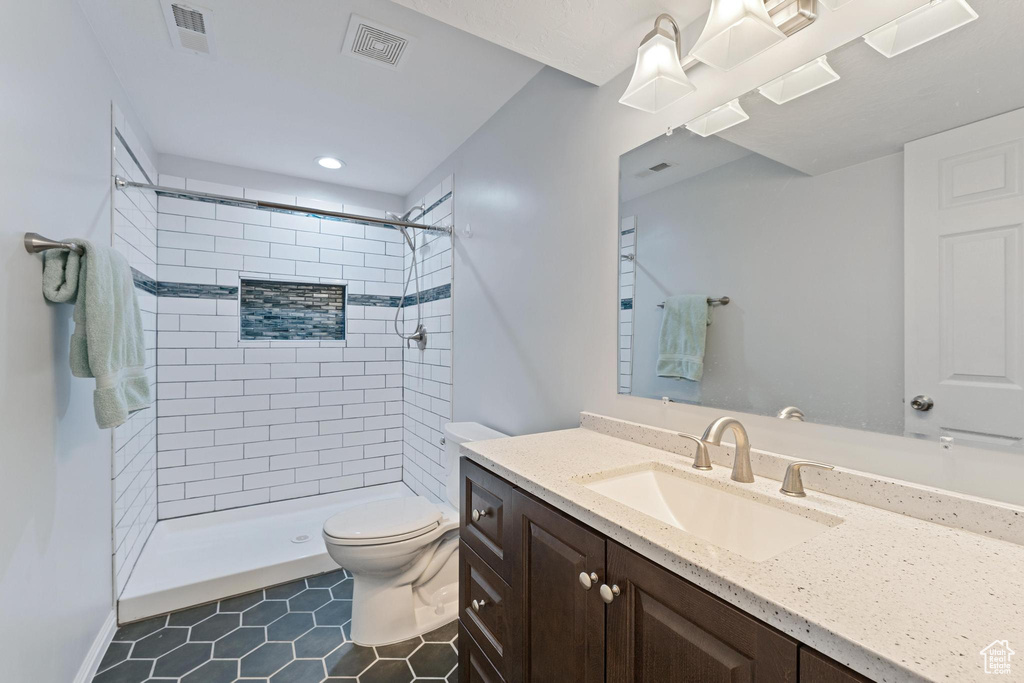 Bathroom featuring tiled shower, tile patterned floors, vanity, and toilet