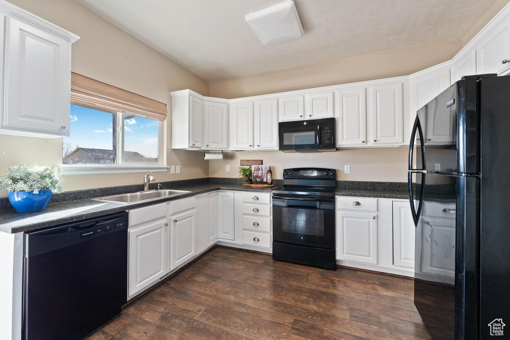 Kitchen with dark wood-type flooring, sink, white cabinets, and black appliances