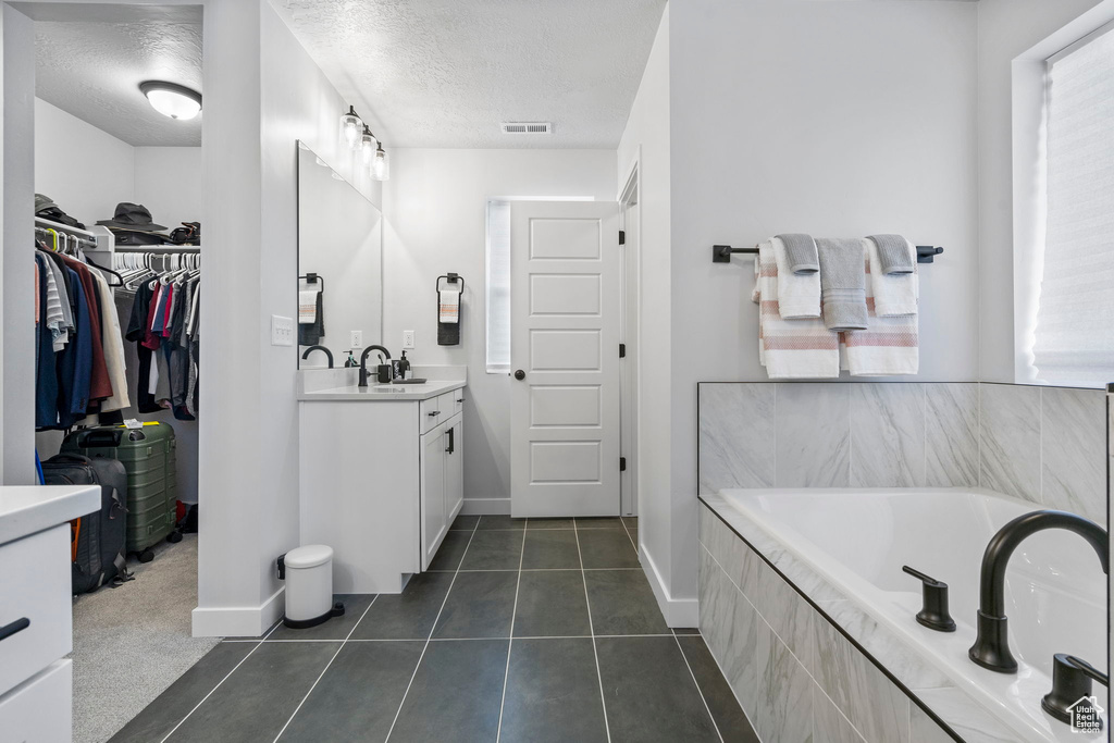 Bathroom with tile patterned flooring, vanity, a relaxing tiled tub, and a textured ceiling