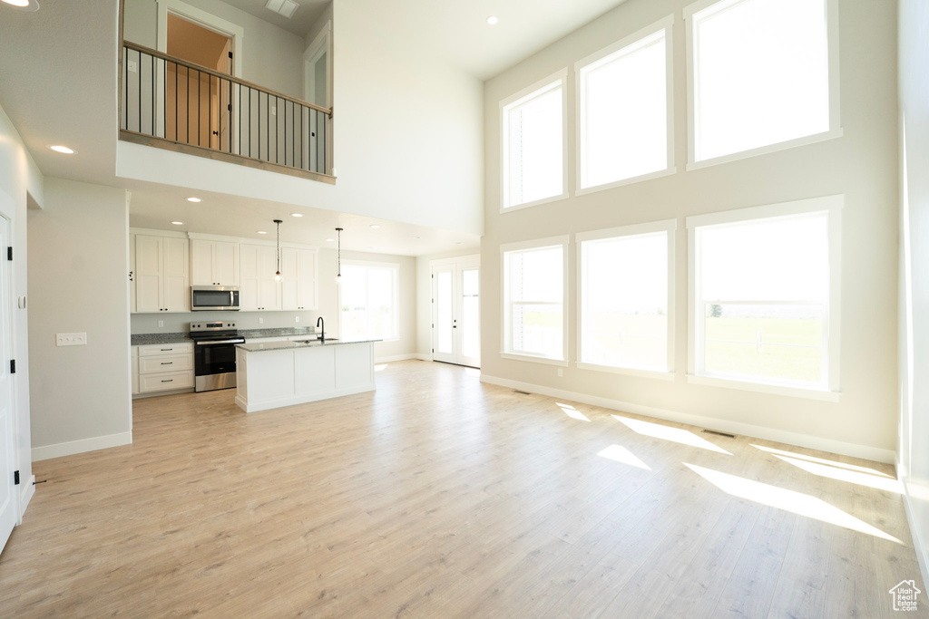 Unfurnished living room featuring a towering ceiling, baseboards, light wood-type flooring, and a sink