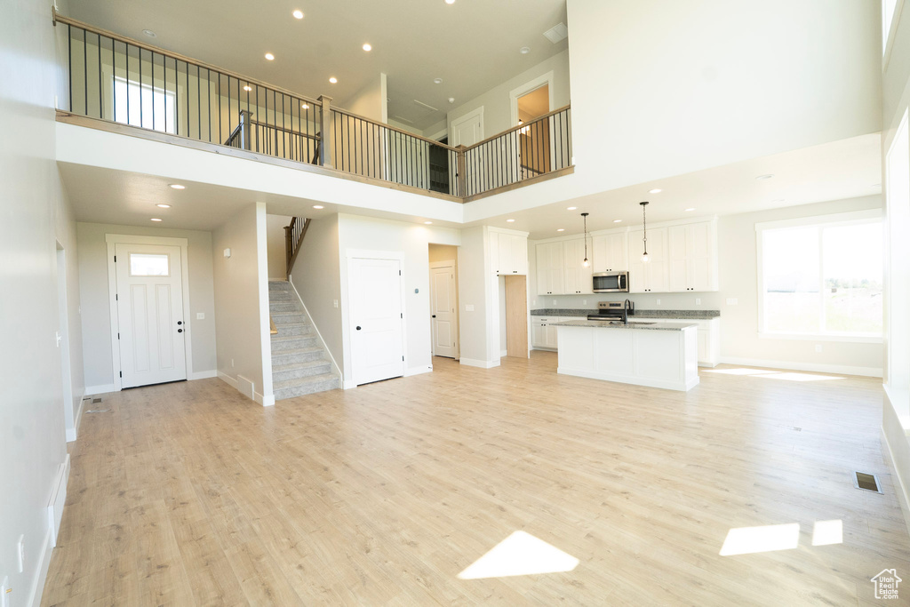 Unfurnished living room featuring a towering ceiling, stairs, light wood-style flooring, baseboards, and recessed lighting