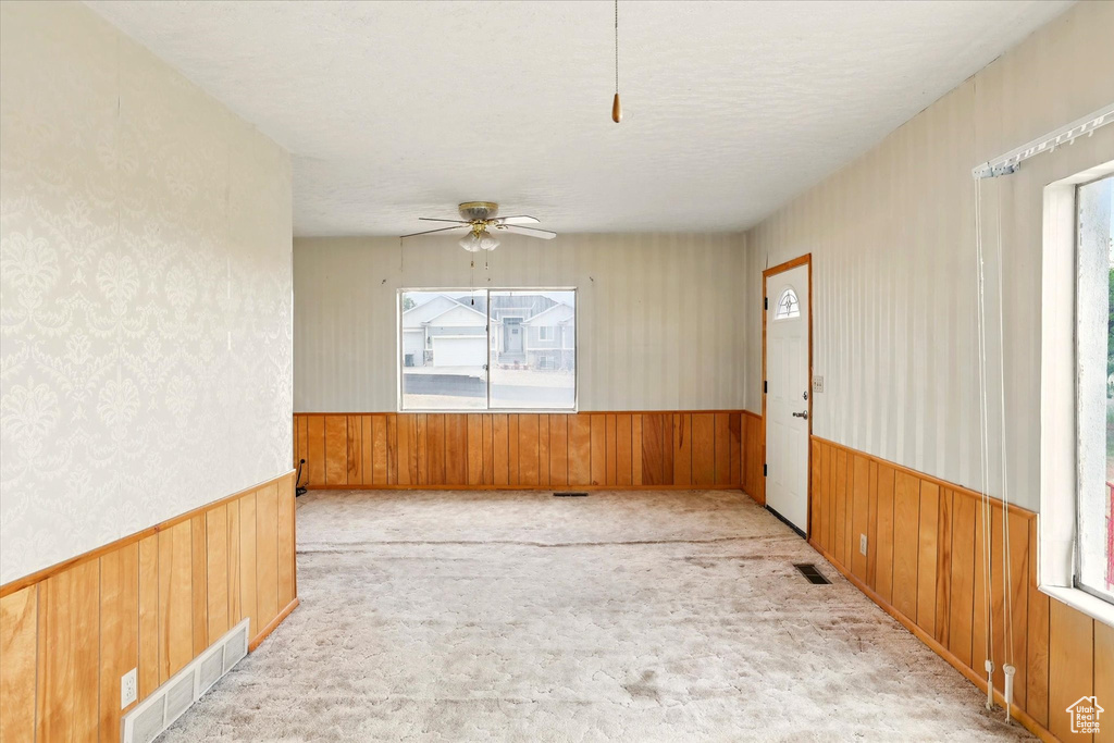 Carpeted empty room featuring wainscoting, wood walls, and ceiling fan