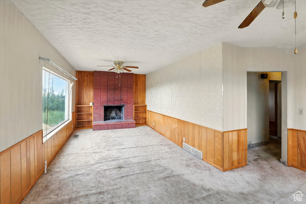 Unfurnished living room with a ceiling fan, a textured ceiling, carpet floors, wooden walls, and wainscoting