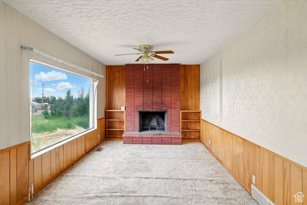 Unfurnished living room with a brick fireplace, plenty of natural light, a textured ceiling, ceiling fan, and wooden walls