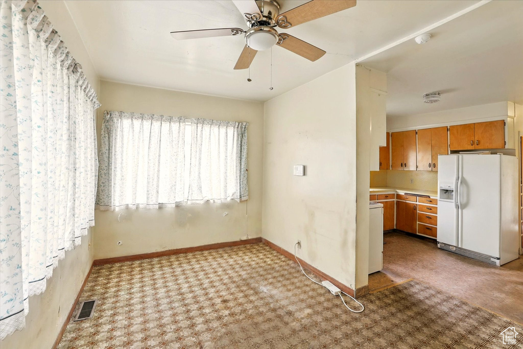 Kitchen featuring white refrigerator with ice dispenser, carpet floors, light countertops, brown cabinetry, and baseboards