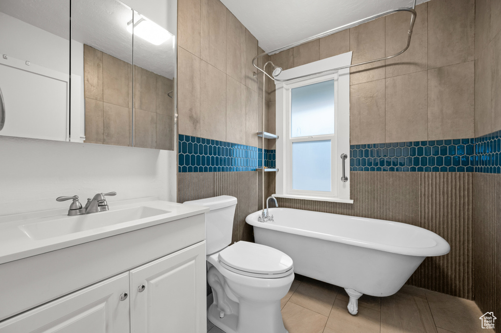 Bathroom featuring tile patterned floors, toilet, a bathtub, vanity, and tile walls