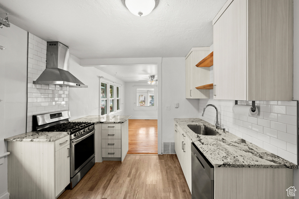 Kitchen with light stone countertops, appliances with stainless steel finishes, decorative backsplash, wall chimney exhaust hood, and sink