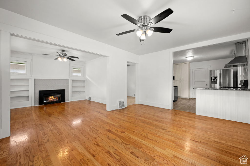 Unfurnished living room with a fireplace, ceiling fan, built in features, and light hardwood / wood-style floors