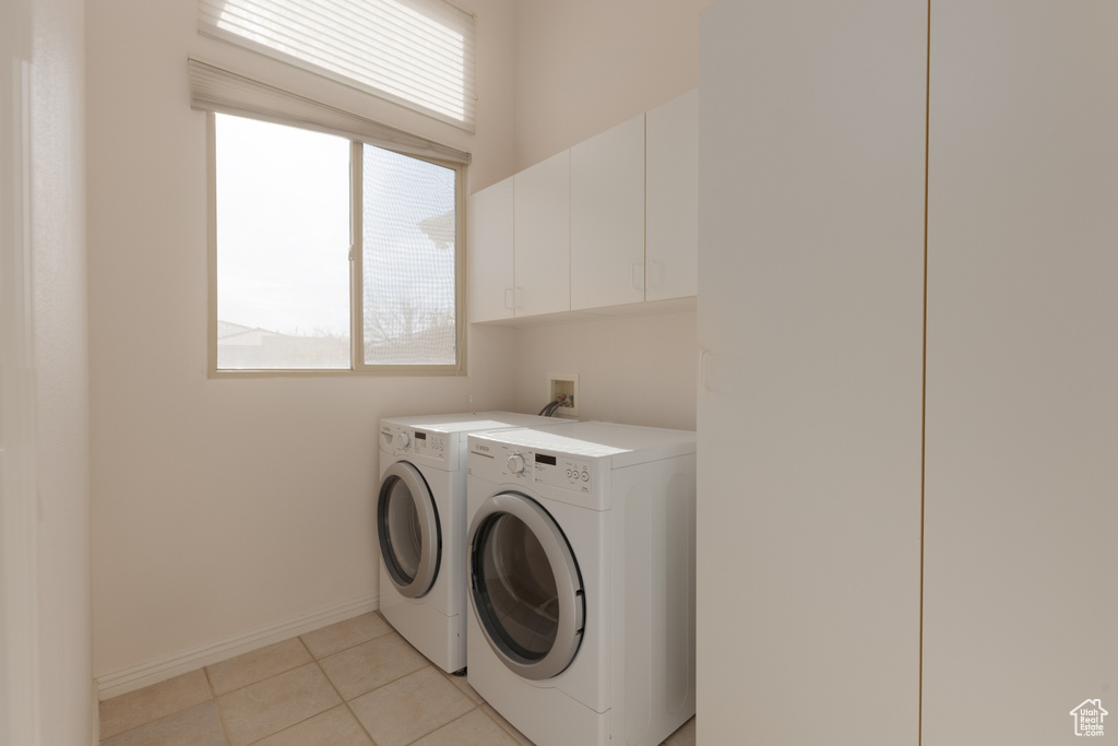 Washroom featuring cabinets, light tile patterned floors, and washing machine and clothes dryer