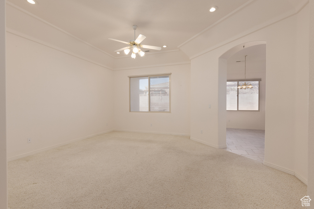 Carpeted spare room with ceiling fan with notable chandelier and ornamental molding