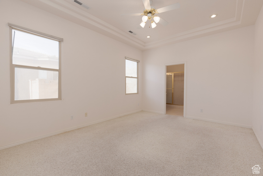 Empty room featuring a tray ceiling, ceiling fan, and light colored carpet