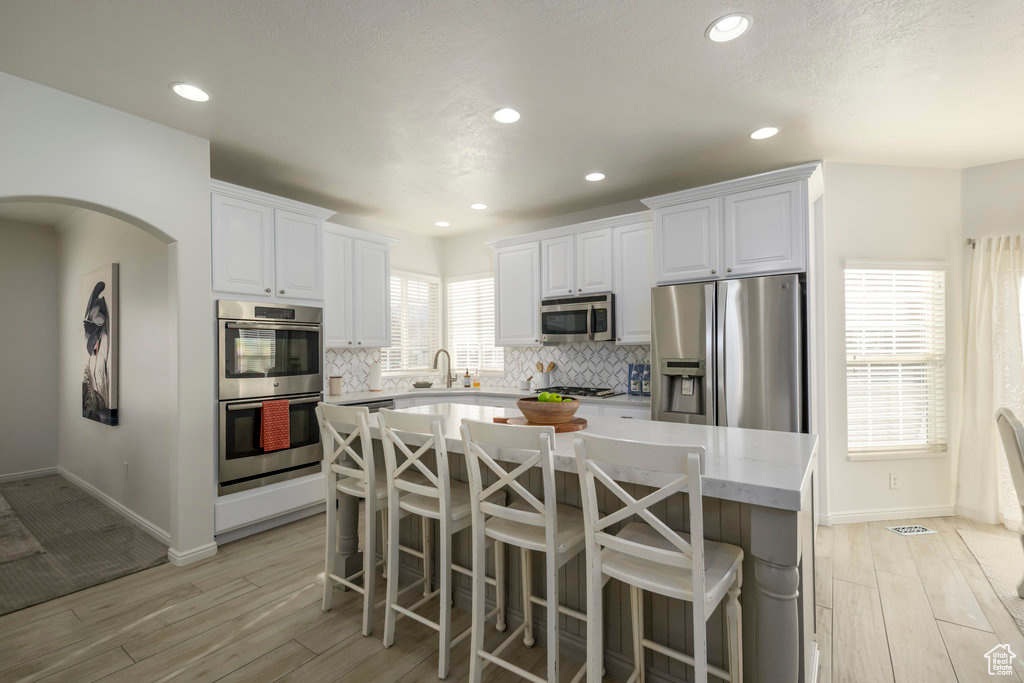 Kitchen with a center island, stainless steel appliances, backsplash, white cabinets, and light wood-type flooring