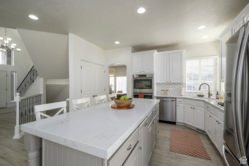 Kitchen featuring appliances with stainless steel finishes, sink, white cabinets, a kitchen island, and hanging light fixtures