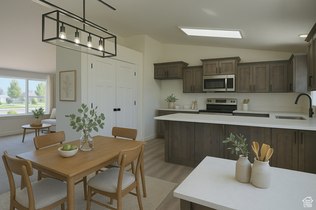Kitchen with dark brown cabinets, appliances with stainless steel finishes, a sink, light countertops, and vaulted ceiling