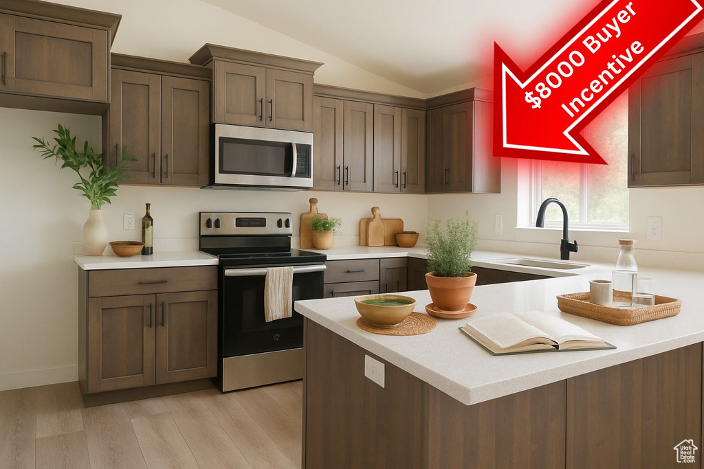 Kitchen featuring light countertops, stainless steel appliances, vaulted ceiling, and a sink