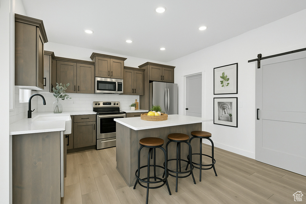 Kitchen with appliances with stainless steel finishes, decorative backsplash, a breakfast bar, and light wood finished floors