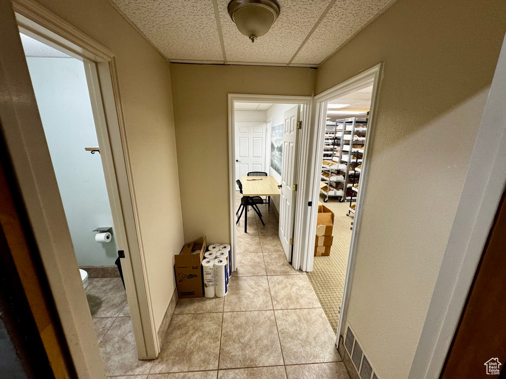 Hall featuring a paneled ceiling and light tile patterned flooring