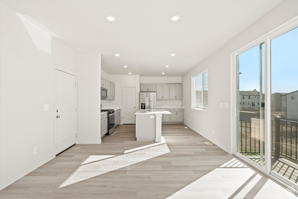Kitchen with appliances with stainless steel finishes, light wood-style floors, light countertops, an island with sink, and recessed lighting