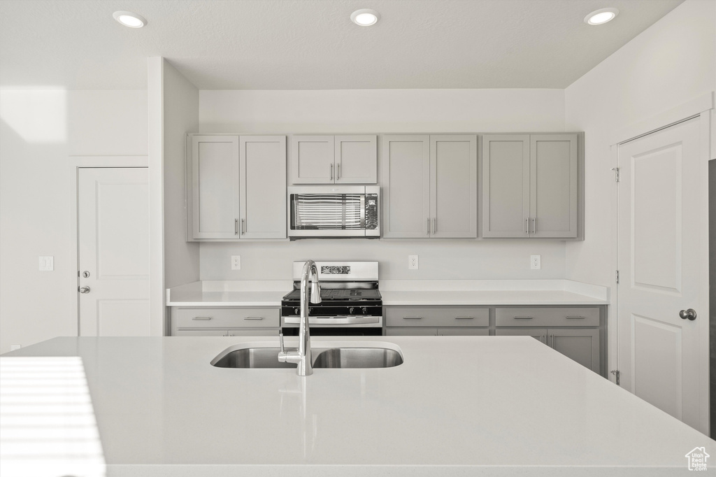 Kitchen with stainless steel appliances, gray cabinets, light countertops, recessed lighting, and a kitchen island with sink